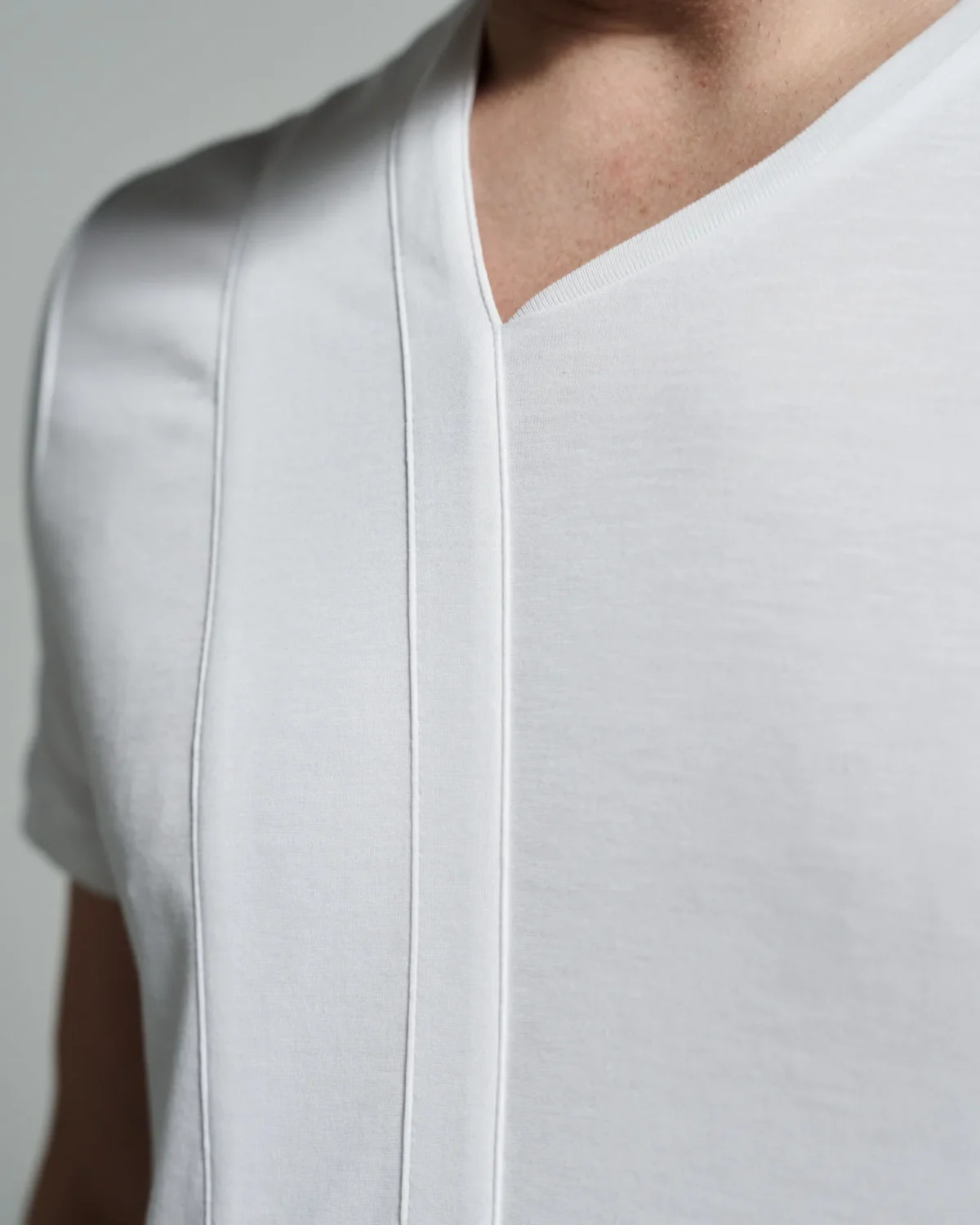 A close-up view of a white T-shirt with an asymmetric crew neck design featuring a sleek strip body detail, highlighting the precision in the stitching and the smooth texture of the fabric.