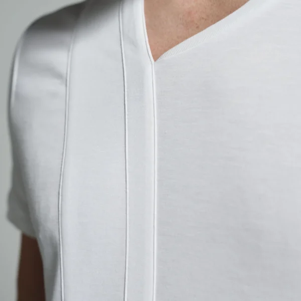 A close-up view of a white T-shirt with an asymmetric crew neck design featuring a sleek strip body detail, highlighting the precision in the stitching and the smooth texture of the fabric.