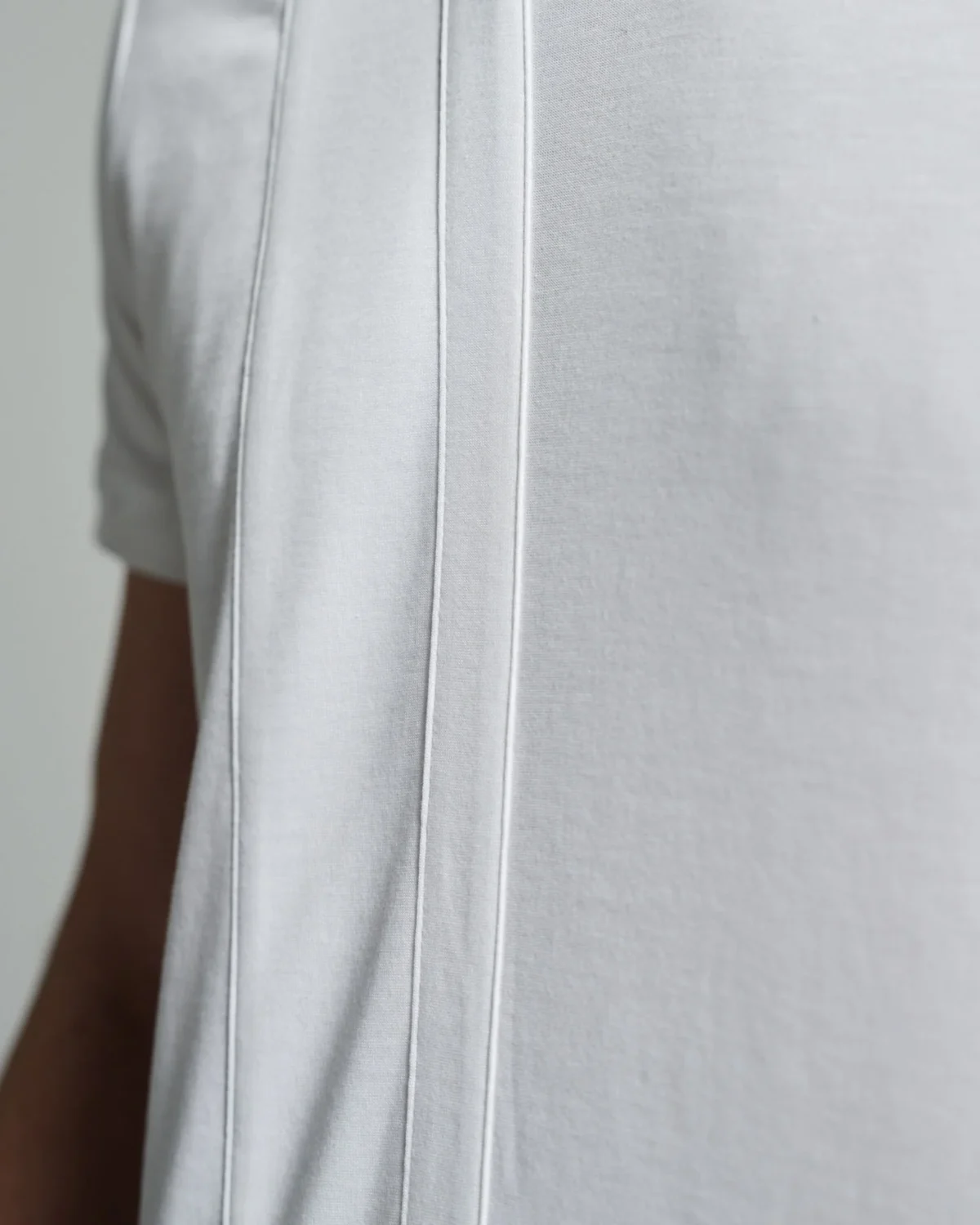 Side view of the white T-shirt showcasing the clean lines and strip body detail running down from the shoulder, emphasizing the minimalistic design and structured fit of the garment.