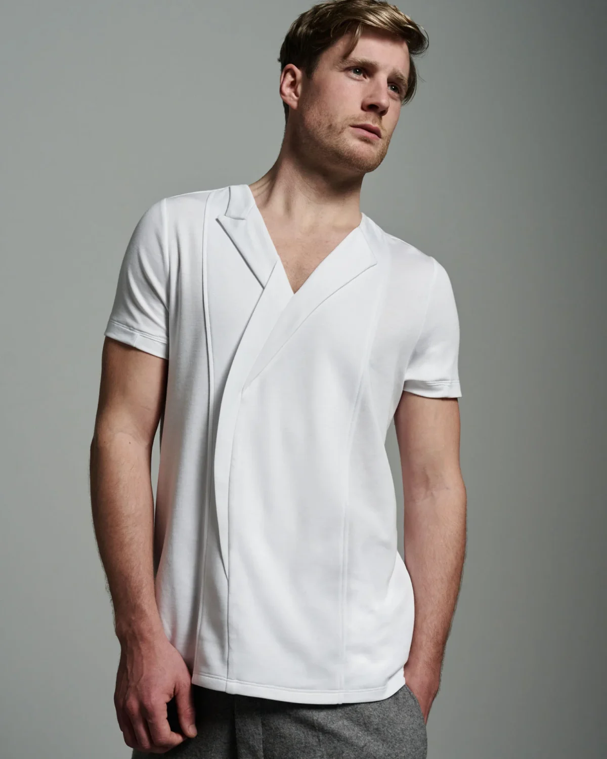 A full-body view of the W. Rubens 73 white T-shirt, modeled to show its full silhouette and design. The asymmetric lapels and inserts create a dynamic front, while the overall fit highlights the shirt’s slim, tailored cut. The model’s pose illustrates the versatility of the piece, suitable for both casual and more formal settings, embodying the quiet luxury W. Rubens is known for